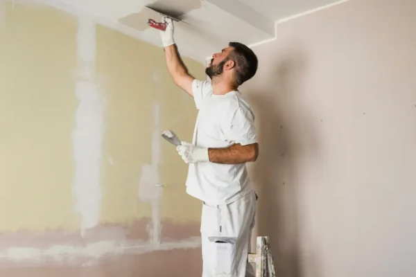 Plasterer applying compound to ceiling joints using a trowel.