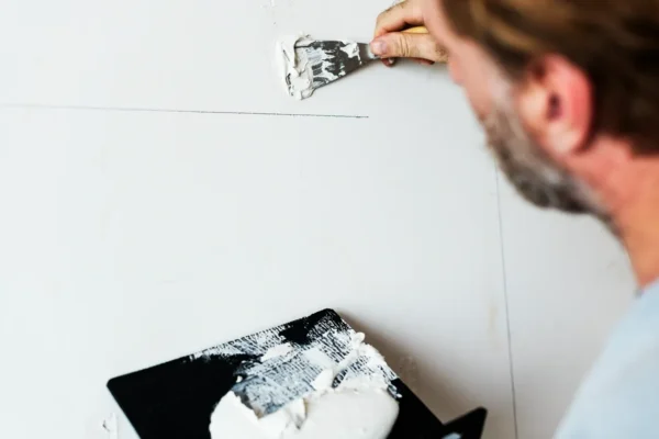 Hand using a trowel to smooth plaster along an internal wall corner.