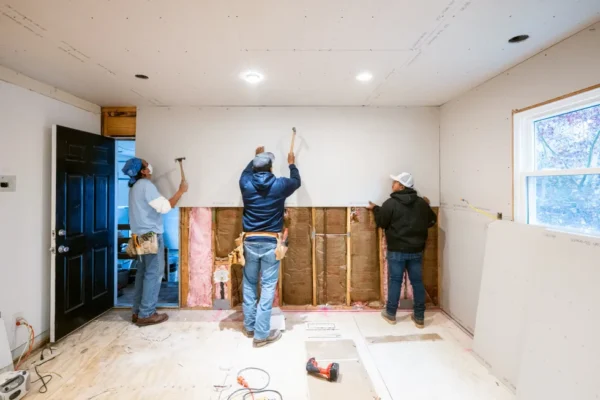 Workers installing drywall sheets and framing interior wall.