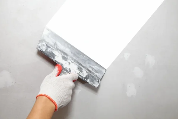 Close-up of plasterer applying filler to wall using a putty knife.