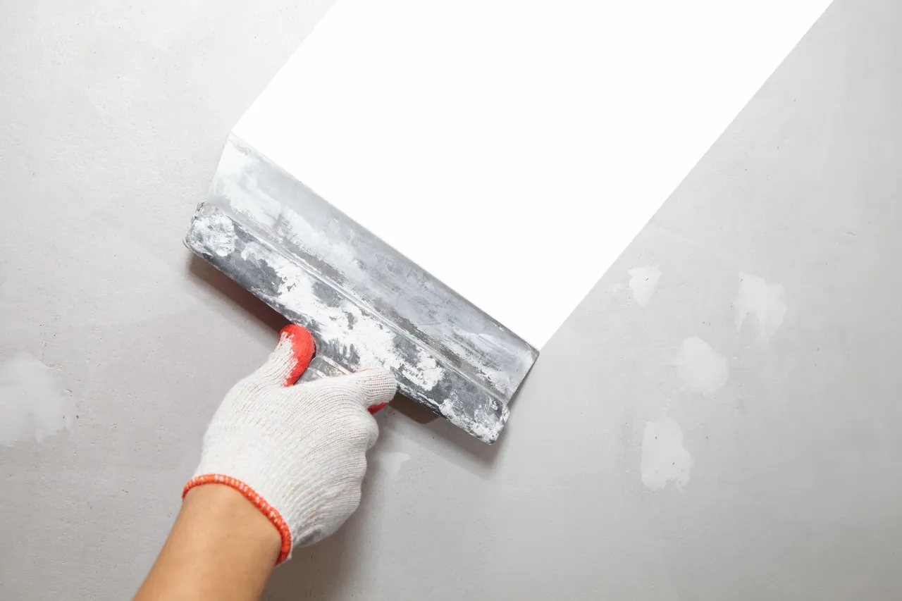 Close-up of plasterer applying filler to wall using a putty knife.