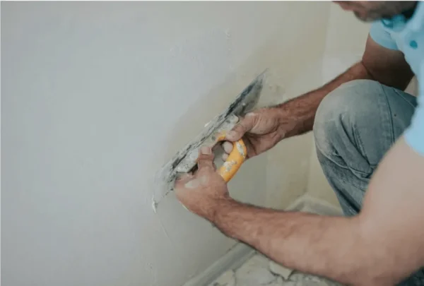Plasterer using a trowel to smooth wall surface during finishing stage.
