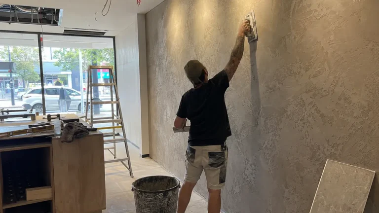 Commercial plasterer applying and smoothing plaster on a feature wall inside a retail shop fit-out.