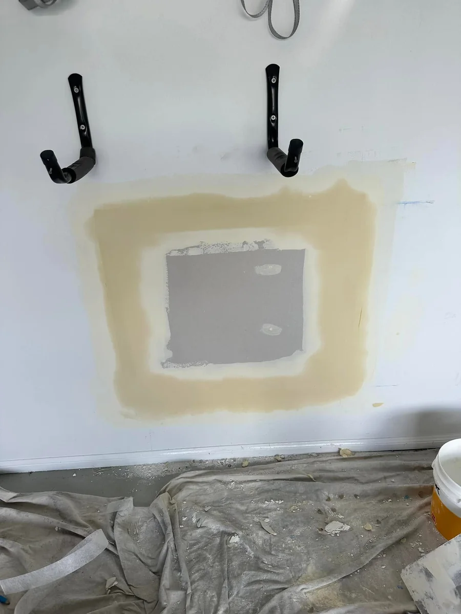 Square plasterboard patch over a large hole in a plaster wall, with base coat feathered out past the edges
