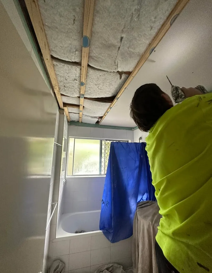 Plasterer repairing a bathroom ceiling with the old sheet removed and the timber battens showing